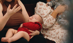 Baby in a red outfit being held by an adult in a casual setting