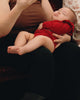 Baby in a red outfit being held by an adult